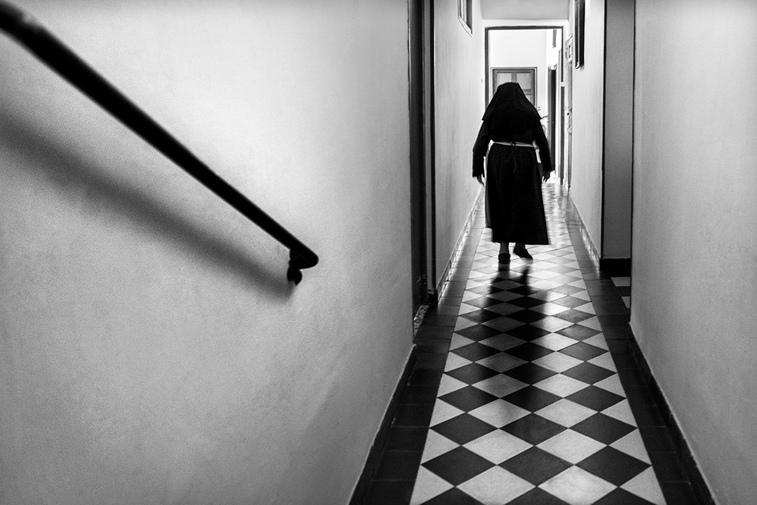 A nun walking along a corridor with a chequered floor.